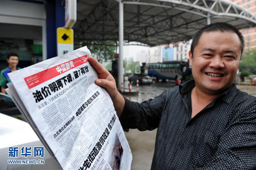 Mr. Jiang reads news of fuel price cuts at a gas station on Donghai Road in Qingdao City, east China's Shandong Province, July 10, 2012. 