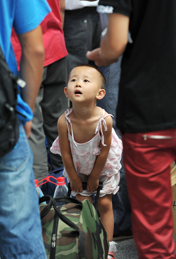 A child tries to carry a luggage in the Yinchuan Railway Station on July 11. The volume of passenger traffic reaches its climax as school vacation and summer workers recruiting start in July. [Xinhua photo] 