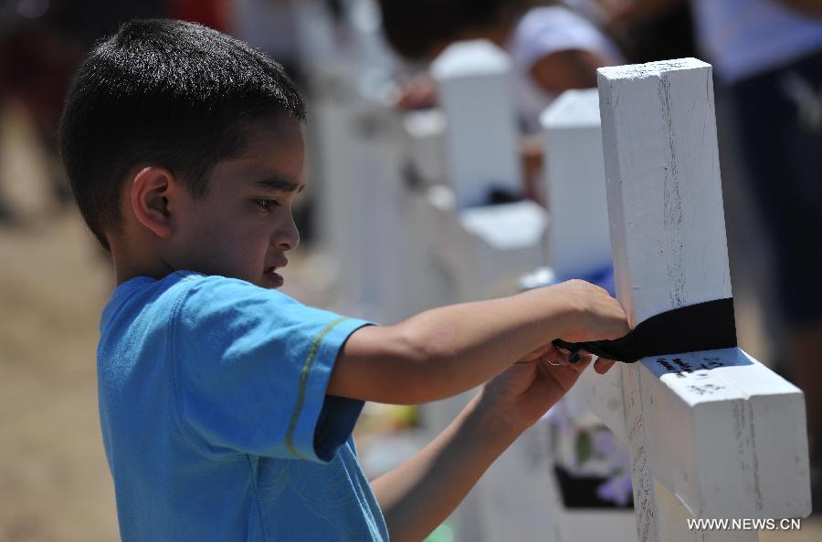 Emma Brazelton ties a black riband on the cross at a memorial near the Century 16 movie theater in Aurora, Colorado, July 22, 2012. Twelve people were killed and 59 others injured at a Batman movie premier, where a lone, heavily armed gunman burst into a packed theater in a suburb 10 miles east of Denver during the wee hours of Friday. (Xinhua/Yang Lei) 