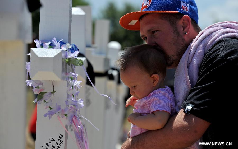 A father and little daughter place a wreath on the cross at a memorial near the Century 16 movie theater in Aurora, Colorado, July 22, 2012. Twelve people were killed and 59 others injured at a Batman movie premier, where a lone, heavily armed gunman burst into a packed theater in a suburb 10 miles east of Denver during the wee hours of Friday. (Xinhua/Yang Lei) 