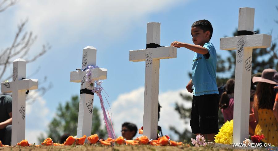 Emma Brazelton ties a black riband on the cross at a memorial near the Century 16 movie theater in Aurora, Colorado, July 22, 2012. Twelve people were killed and 59 others injured at a Batman movie premier, where a lone, heavily armed gunman burst into a packed theater in a suburb 10 miles east of Denver during the wee hours of Friday. (Xinhua/Yang Lei) 