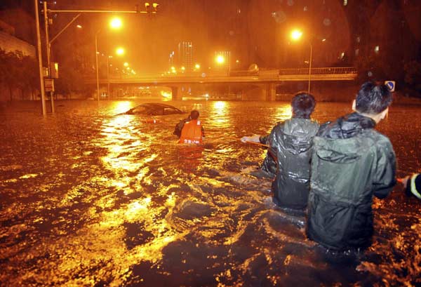 Rescuers and residents stand next to a stranded car which is being pulled up from a flooded street under the Guangqumen overpass amid heavy rainfall in Beijing, July 21, 2012.[ Photo / China Daily ]