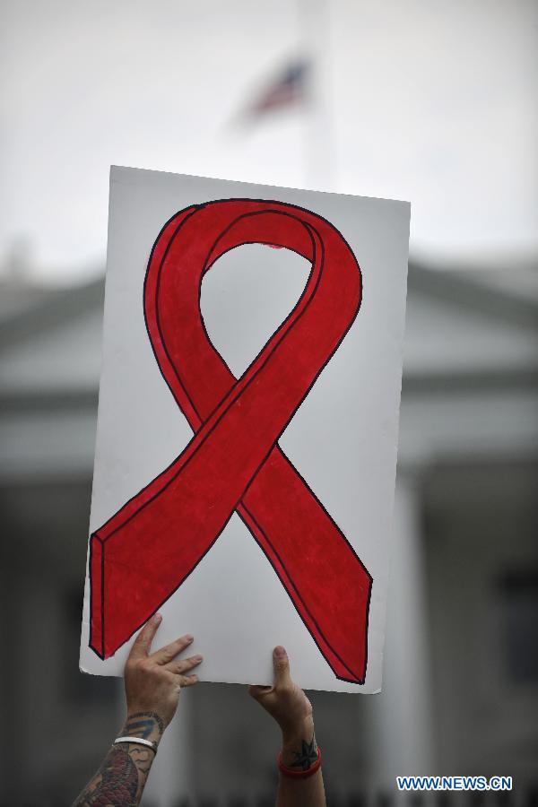A protestor holds a placard depicting a red ribbon outside the White House during AIDS Parade in Washington D.C., capital of the United States, July 24, 2012. Thousands of people gathered around the Washington Convention Center where the 19th International AIDS Conference is convened and walked to the White House, asking the U.S. governmant for more attention to AIDS medical care and elimination of the discrimination against HIV Possitives. (Xinhua/Zhang Jun) 