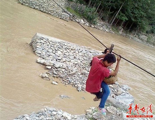 Students in Wen County, Gansu province, use a cable to cross the Bailong River on their way to school. [Photo: voc.com.cn]