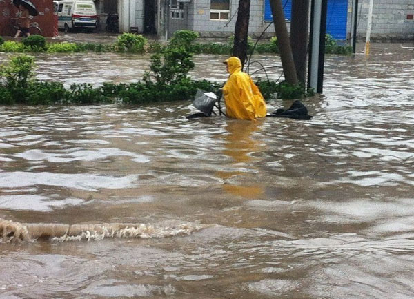 A person on a bicycle is stuck in water up to their waist in the floods in Tianjin, on July 26. [ Photo / ynet.com ]