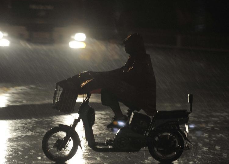 A citizen rides in rain under the Jingtai overpass in downtown Beijing, capital of China, July 27, 2012. A new round of torrential rain pelted the capital Friday evening. 