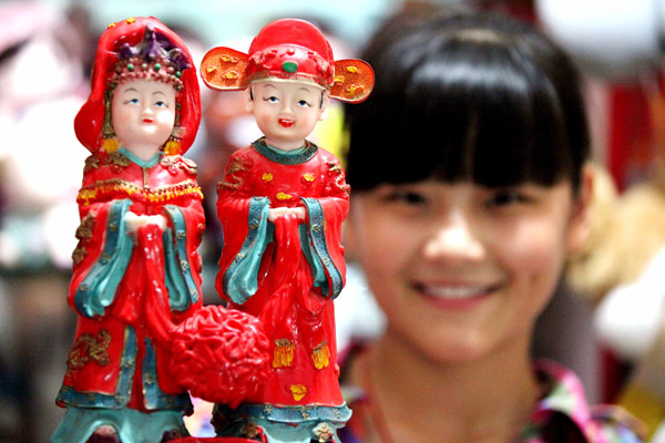 A woman shows traditional decorations for a Chinese wedding ahead of the upcoming Qixi Festival in a shop in Bozhou, Anhui province, Aug 5. [Photo by Liu Qinli/Asianewsphoto]