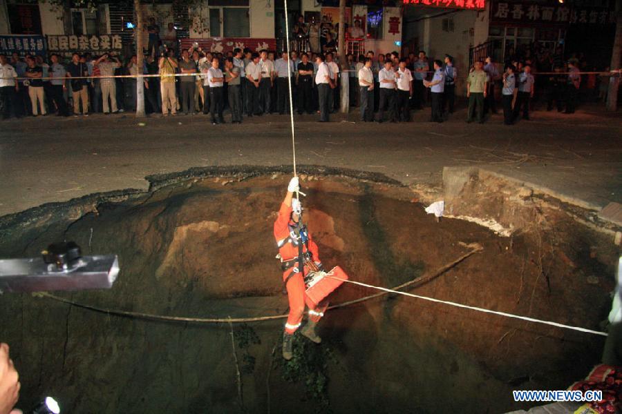 A firefighter rescues citizens at an accident site after a road collapsed at Liaoyang Street of Harbin City, northeast China's Heilongjiang Province, Aug. 14, 2012. Two people were confirmed dead and two others injured when a roadbed collapsed at Liaoyang Street in Nangang District of Harbin City on Tuesday. 