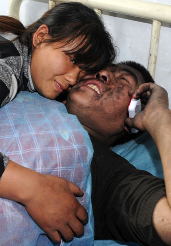 Coal miner Wang Qiming talks to his father on the phone on Friday, while his wife comforts him, after he was rescued in Fugu, Shaanxi province. Wang and 14 of his colleagues were rescued after a roof collapsed at the mine while 96 miners were working underground. One miner is still missing. [Photo / Xinhua]