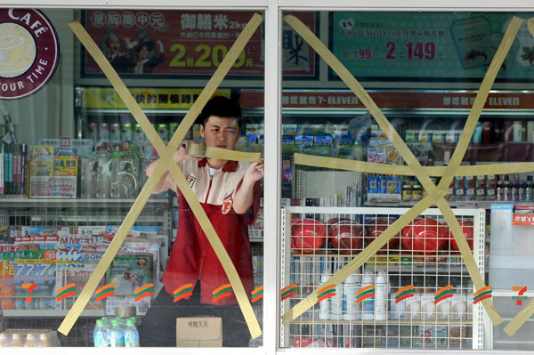 A worker tapes the window of a convenience store in Hualien, Taiwan province, on Wednesday, in preparation for typhoon Tembin. [Photo/China Daily]