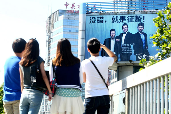Pedestrians look at a billboard displaying the photos and personal information of three bachelors' seeking marriage, in Beijing's Zhongguancun last week. Fu Ding / for China Daily