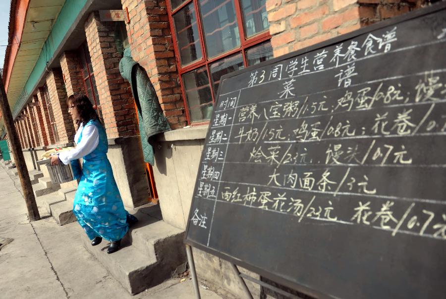 A teacher carries students' lunch out of the kitchen with the foreground showing a blackboard written with the menu of the students, at Shimen central primary school in Tianzhu Tibetan Autonomous Prefecture, northwest China's Gansu Province, March 12, 2012. 
