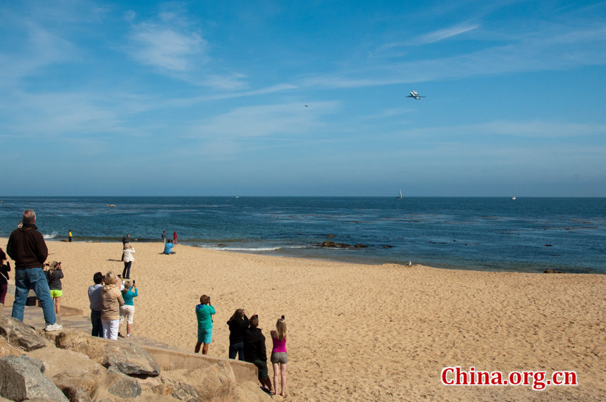 The Endeavour, strapped to the back of a NASA's modified Boeing 747, attracts huge applauses from watchers when it comes into view during its flyover at the Fishermen's Wharf, Monterey on Friday. Citizens and tourists at the scene both document the moment either with cameras or iPhones. [Chen Boyuan/China.org.cn]