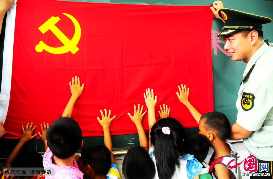 2012年9月1日，听了边防警察叔叔的介绍，小同学们争相把小手伸向党旗。[中国网图片库 周炜摄影]