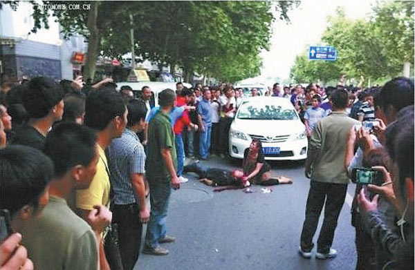 Attacked by anti-Japanese protestors, a severely injured Li Jianli lies in front of his Toyota with his wife at his side in downtown Xi’an, Shaanxi province, on Sept 15. PROVIDED TO CHINA DAILY    