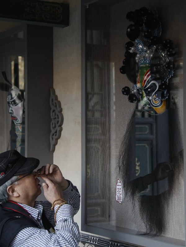 A tourist looks at a facial mask of Beijing Opera in north China&apos;s Shanxi Province, Sept. 28, 2012. The cultural tourism programs promoted by Jinzhong City have attracted many visitors from home and abroad.