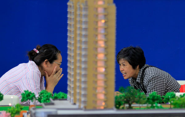 Visitors talk beside a building model at a real estate trade fair in Nanjing, Jiangsu province, in September. [Photo/China Daily]