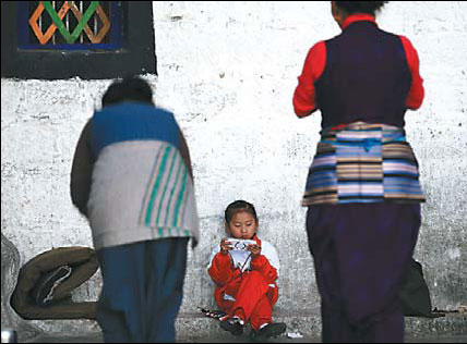 A girl plays a game on her PlayStation Portable console while her family members are praying outside the Jokhang Temple, Lhasa, on Sept 28. [Photo / China Daily]