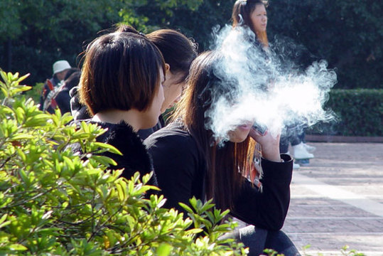 A woman is obscured by a cloud of smoke as she enjoys a cigarette alongside a group of non-smokers in a park in Wuhan, capital of Hubei province, on Sunday. [China Daily]