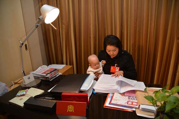 Luo Wei, a deputy to the 18th National Congress of the Communist Party of China, reads congress material while taking care of her five-month-old daughter at a hotel in Beijing on Nov 10, 2012. [Photo/Asianewsphoto]