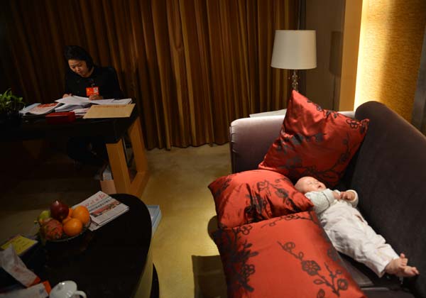 Luo Wei, a deputy to the 18th National Congress of the Communist Party of China, reads congress material while her five-month-old daughter sleeps at a hotel in Beijing on Nov 10, 2012. [Photo/Asianewsphoto]