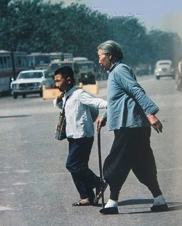 A small-footed elderly lady, assisted by her grandson, crosses the Chang'an Avenue.