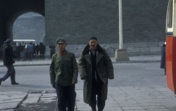 A soldier walks on the street, followed by his father who wears a military coat probably given to him by his son.