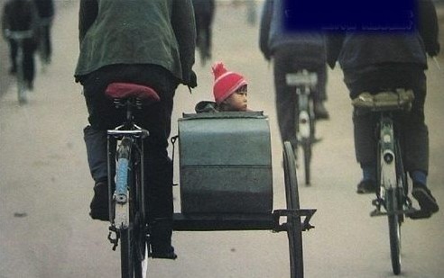 A small child sticks his head out of a sidecar attached to a bicycle.