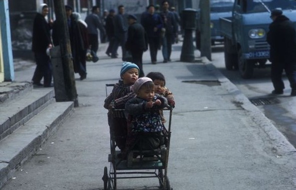 Three young children are crammed in a baby trolley.