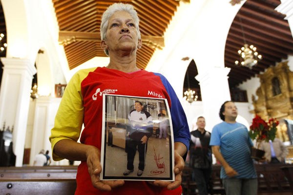 A supporter of Venezuelan President Hugo Chavez holds a picture of him, as she attends a mass to pray for Chavez's health in Caracas Dec 24, 2012. [Photo/Agencies]    