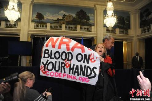 A gun-control activist holds a slogan against  the National Rifle Association in its new conference on Dec 21, 2012. [Chinanews.com]