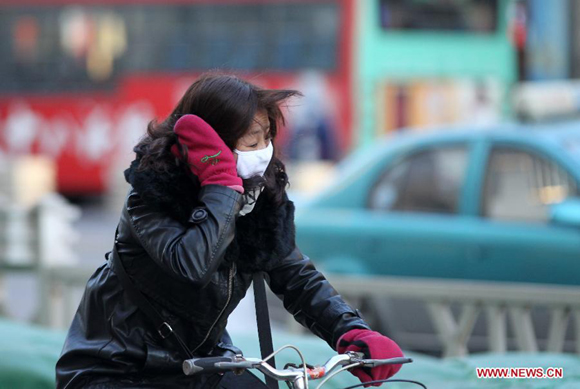 A woman rides a bike against the wind in Qinhuangdao, north China's Hebei Province, Dec. 23, 2012. A severe cold wave is sweeping most parts of China, with temperatures dropping by around 10 degrees Celsius in some areas. The local meteorological authority issued a blue alert for the cold wave on Sunday.