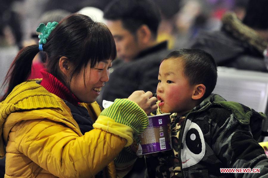 A woman feeds instant noodles to her child at the waiting hall of railway station in Ji'nan, capital of east China's Shandong Province, Jan. 26, 2013. The 40-day Spring Festival travel rush started Saturday. [Cui Jian/Xinhua]