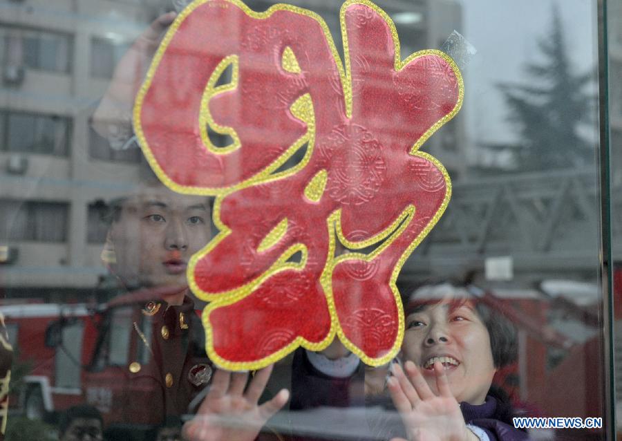 Hao Min (R), a community worker, attaches a paper-cut ornament in the shape of Chinese character 'Fu', or happiness in English, onto windows together with firefighter Han Xiaoyu at a fire brigade in Wulidun Community of Hefei, capital of east China's Anhui Province, Jan. 30, 2013. A group of community workers and retired staff members visited Wulidun fire brigade to celebrate the upcoming Spring Festival with the firefighters here on Wednesday. (Xinhua/Guo Chen) 