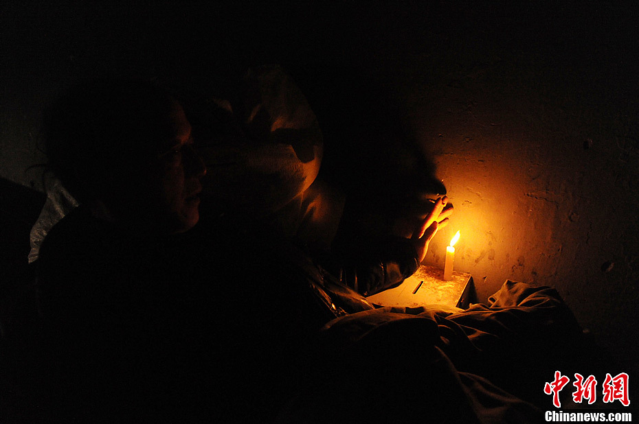 A wanderer tries to warm his hands by a candle. Many wanderers in Changsha City, Hunan Province, choose to celebrate the upcoming Spring Festival under overpasses. Hotpot is the only festive meal they can afford.