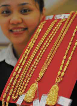 A shop assistant displays gold jewelry in Qionghai, Hainan province, on Thursday. [Photo/China Daily]