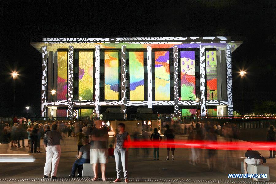 People watch the National Library of Australia as it is illuminated by a large scale projection, in Canberra, Australia, March 9, 2013. 