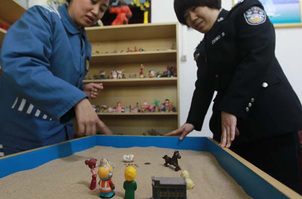 An inmate enjoys a light moment with a corrections officer over a sandbox in Beijing Women's Prison on March 5. [Photo/China Daily]