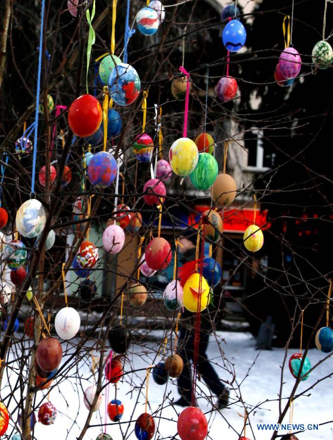 A passer-by walks beside a birch tree with colorful Easter eggs decorations, in front of the Pankow Church, Berlin, March 31, 2013.