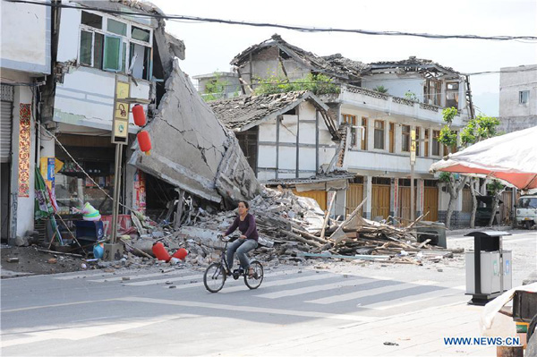 A local resident rides in front of collapsed houses in quake-hit Lushan County, Ya'an City, southwest China's Sichuan Province, April 20, 2013. [Jin Xiaoming/Xinhua]