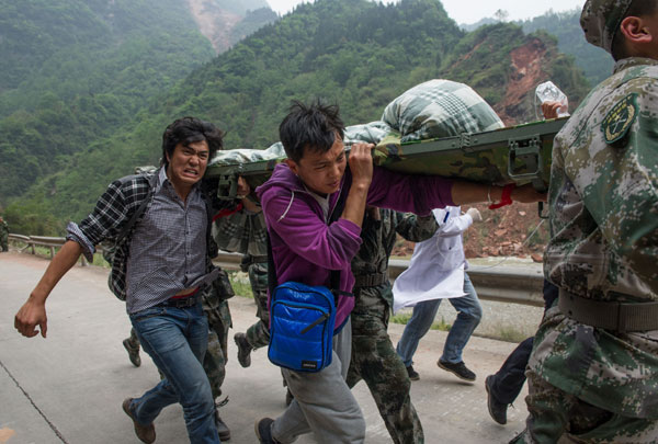 Volunteers Yang Chengcheng (left) and Xiao Long, from Southwest University for Nationalities in Chengdu, join soldiers to rush injured people to an aid center 10 kilometers away in Lushan, Sichuan province, on Sunday. [Photo/Xinhua] 