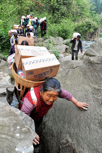 An elderly woman carries a bamboo basket on her back filled with cartons of biscuits and water as she and fellow villagers trudge up a rugged mountain path to bring relief supplies to more than 2,000 residents in Shifeng, a village in Lushan County. 