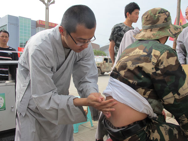 Shi Yanyun, a rescue team member from Shaolin Temple, treats a volunteer who hurt his back during earthquake rescue operations in Lushan, Sichuan province, on Thursday. [Photo/China Daily]