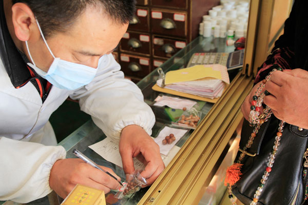 Pharmacist Tenzin writes the name of a traditionally made Tibetan drug on a tag for patients. [Photo / China Daily]