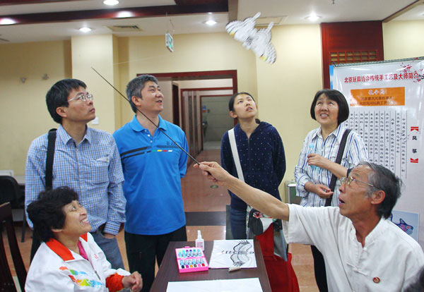 Kong Lingmin (right) shows his traditional kite craftsman skills at a job fair on Sunday, the annual National Day for Helping the Disabled. The job fair is aimed at providing more employment opportunities for disabled people and preserving folk art. [Photo/China Daily]