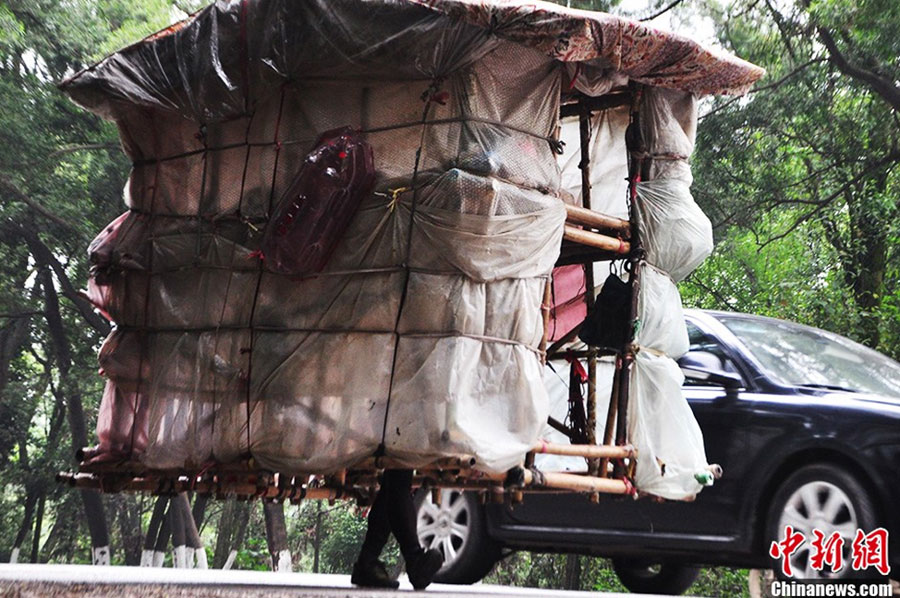 Liu Lingchao walks on a section of National Highway 209 in Liuzhou City with his simple and crude house on his shoulders on Tuesday, May 21, 2013. [Photo/chinanews.cn]
