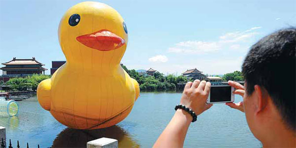 A visitor to Hengdian World Studios in Dongyang, Zhejiang province, takes photos of an inflatable rubber duck. [Photo/China Daily] 