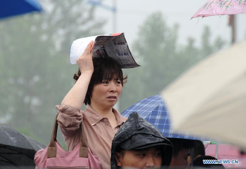 A mother waits under the rain for her kid taking the national college entrance exam in Gu'an, north China's Hebei Province, June 7, 2013. Some 9.12 million applicants are expected to sit this year's college entrance exam.