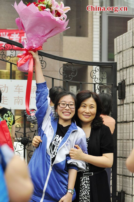 A student carrying a bunch of flowers presented by her parents is posing for souvenir photos with her mother who has been waiting for her outside the school gate. [Photo / Gong Yingchun]