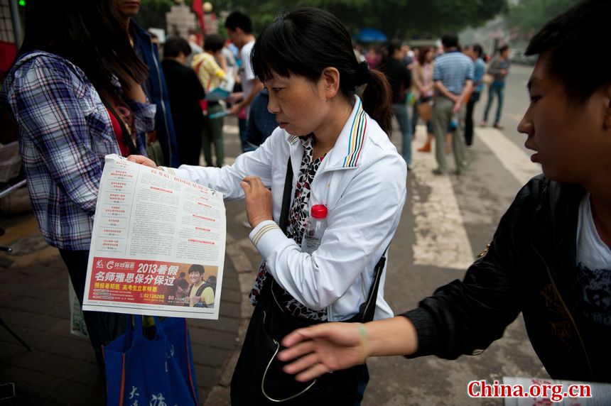 A student&apos;s parent looks at an education agency&apos;s advertisement as she is waiting outside the High School Attached to Capital Normal University on Saturday afternoon. Her child is taking the colleage entrance examination or gaokao, which ends on Saturday, June 8, 2013. [Photo / Chen Boyuan]